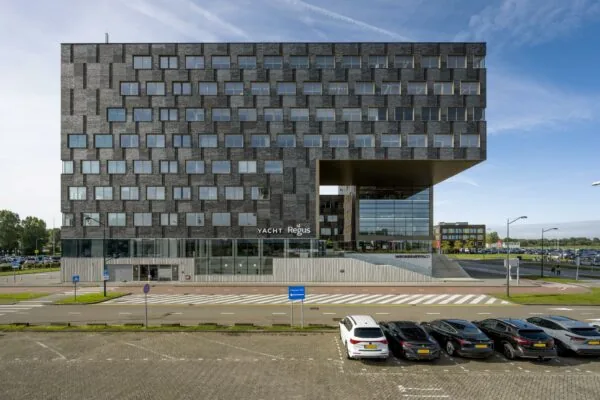 Modern kantoorgebouw aan het Rotterdam Airportplein met opvallende gevel en parkeerplaatsen op de voorgrond.